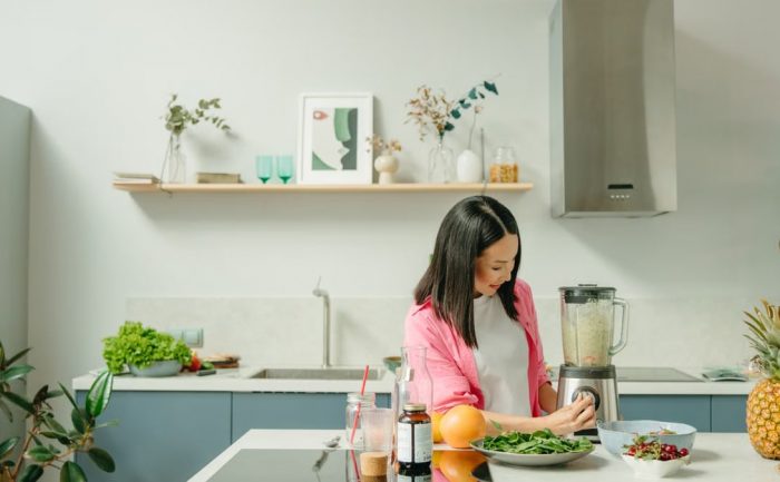 A woman blends fresh ingredients for a healthy smoothie in a stylish kitchen, promoting wellness.